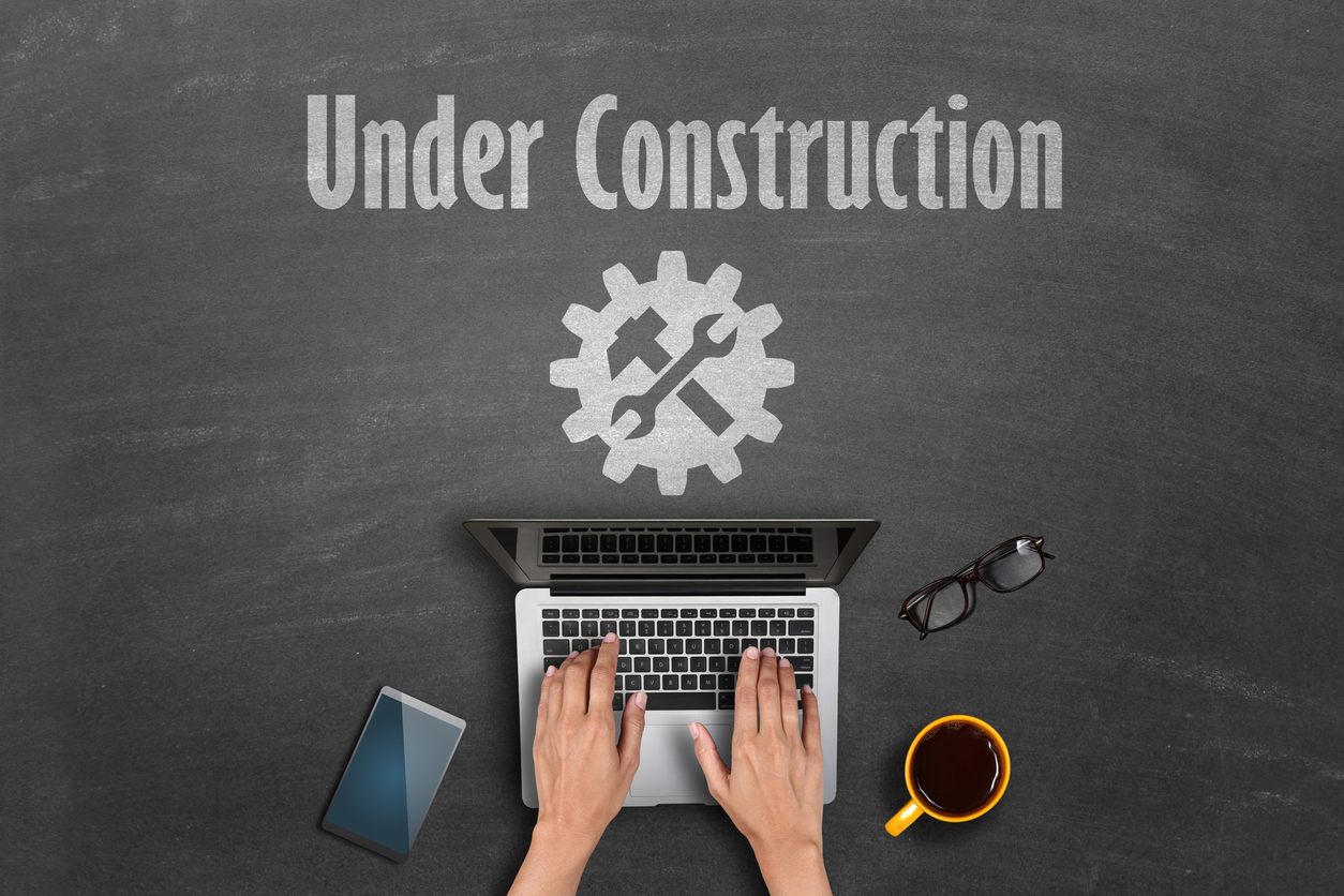 Under construction concept Top shot of person hands working on laptop and under construction text with it support icon drawn on blackboard.