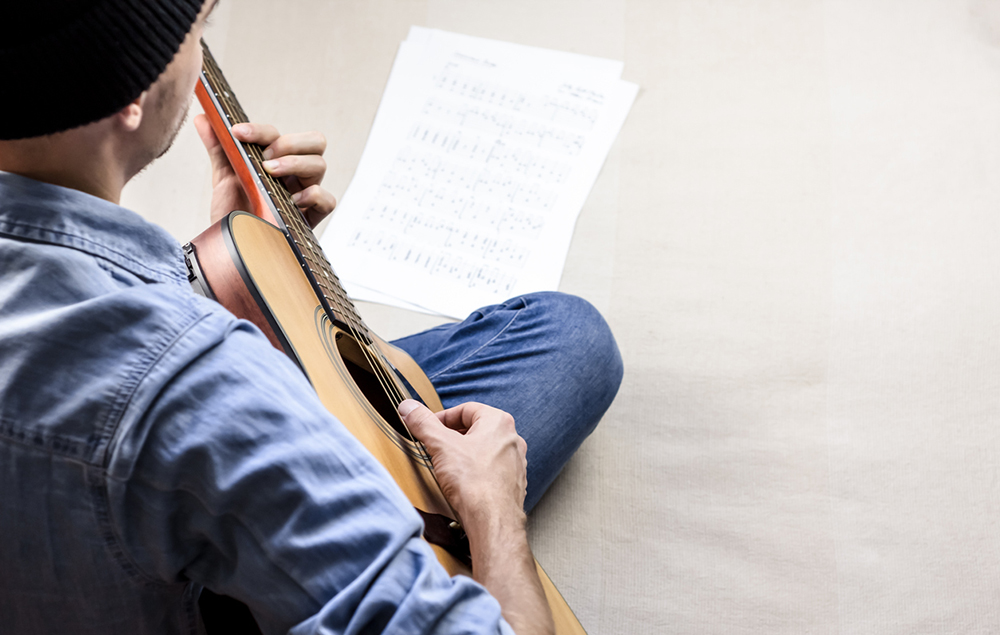 Singer songwriter plays song from sheet music tabs Male guitar player in jeans composing a song on acoustic guitar