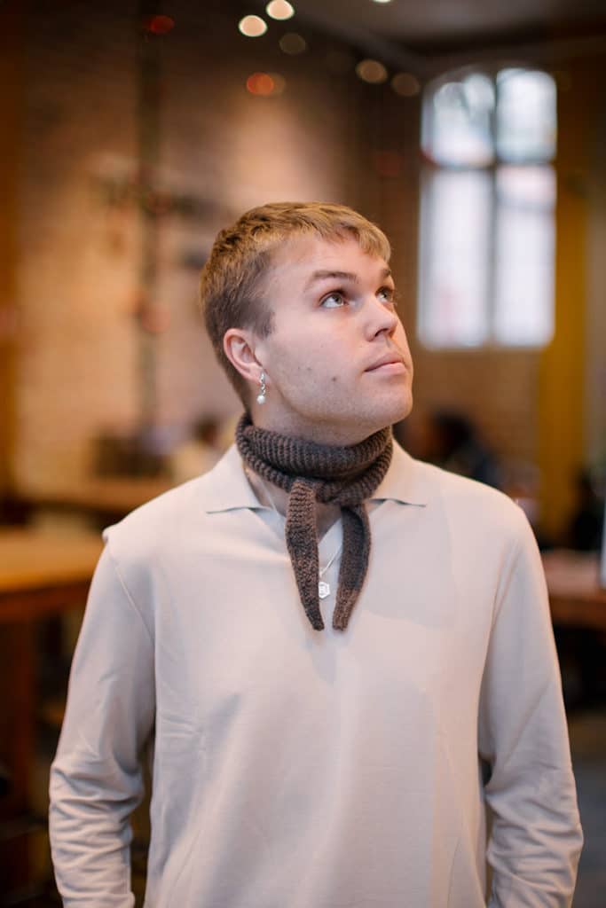 En mann i beige poloskjorte og skjerf står og ser oppover mot den ene siden, i en kafé.