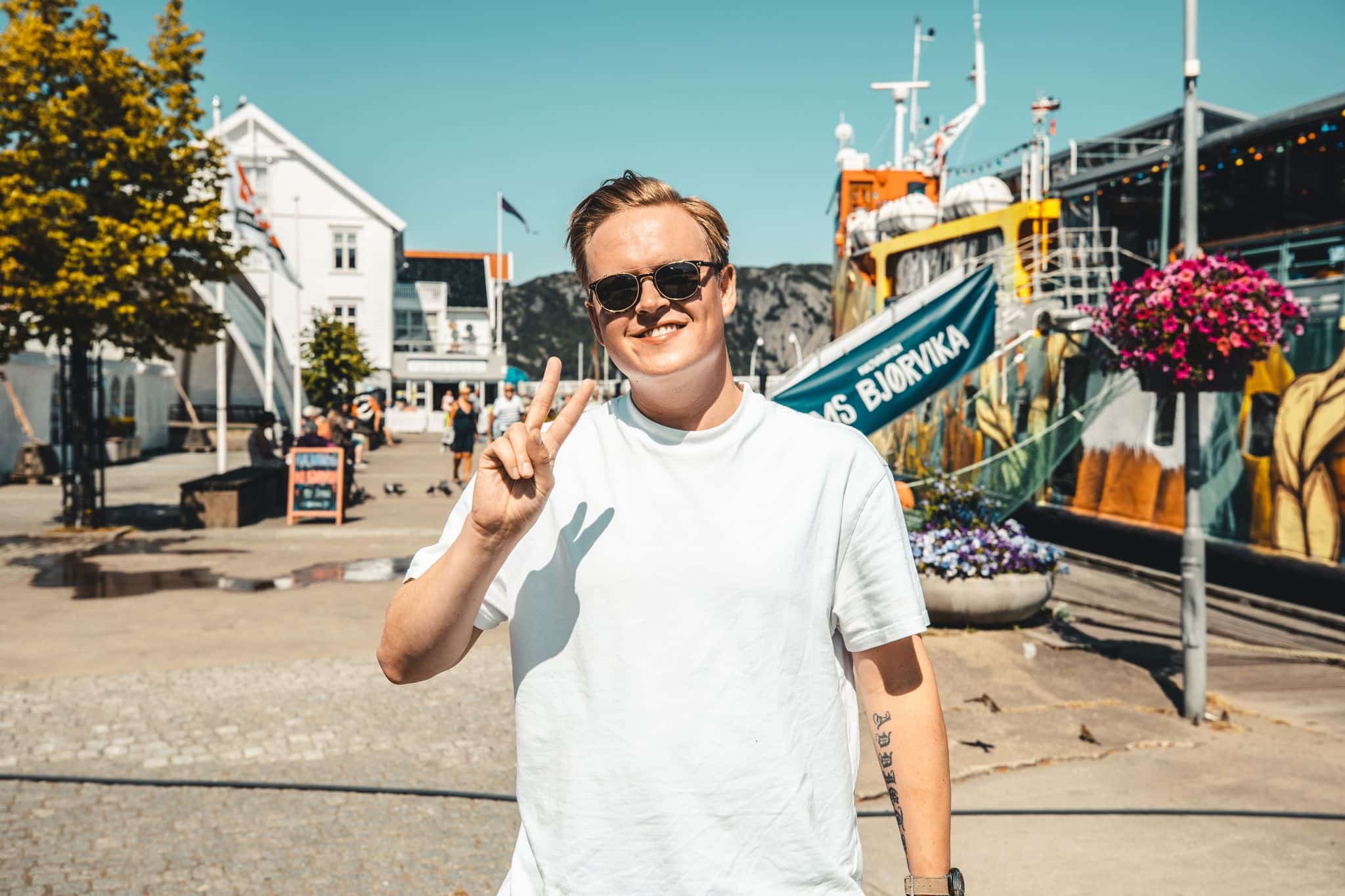TONO_sommerlaater_VidarVilla_1.jpg – En mann med blondt hår, solbriller og hvit t-skjorte gjør fredstegnet.